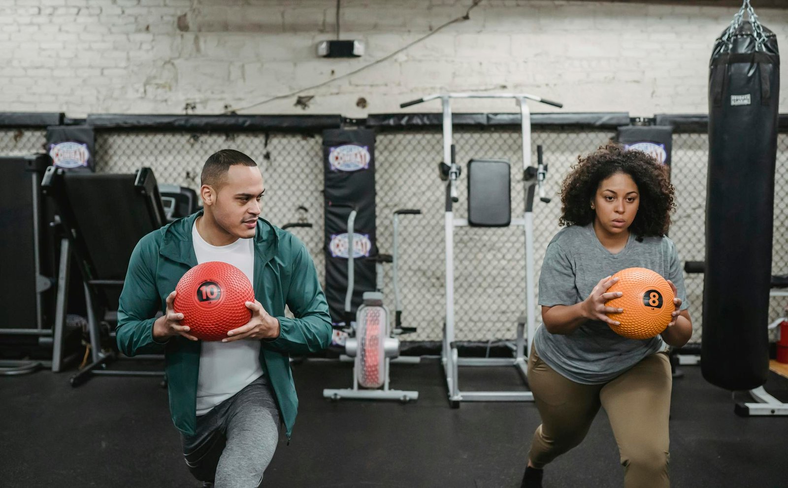 Young muscular ethnic male instructor in activewear doing lunges exercise with ball near plus size black woman during training in sport club